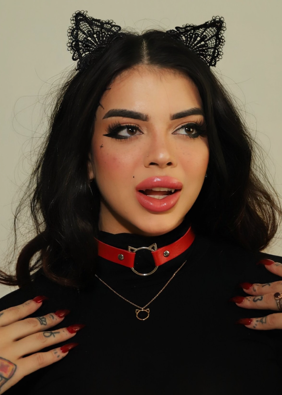 Person wearing black lace cat ears and a red choker with tattoos on hands